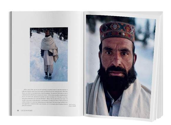 L'image montre une double page d'un livre présentant un récit de voyage ou un reportage photographique.  Sur la page de gauche, un texte décrit un moment ou une rencontre avec un homme dans un environnement hivernal. Une petite photo montre cet homme debout dans la neige, habillé d'une tenue traditionnelle comprenant une longue écharpe ou châle enroulée autour de ses épaules. La scène est probablement capturée dans une région montagneuse ou froide, avec des arbres enneigés visibles à l'arrière-plan. Le texte, bien qu'il ne soit pas complètement lisible, semble offrir des détails sur la rencontre ou sur l'histoire de cet homme.  Sur la page de droite, une grande photographie en couleur offre un portrait saisissant de l'homme. Il porte un chapeau traditionnel brodé, orné de motifs colorés. Son visage est marqué par une barbe épaisse, et son regard intense est dirigé directement vers l'objectif. Le portrait capte l'essence et la dignité de cette personne, tout en reflétant une ambiance paisible et froide avec le paysage enneigé en arrière-plan.  Cette double page associe habilement une description écrite à un puissant visuel, offrant une immersion dans une culture ou une région spécifique. Le contraste entre le paysage hivernal et l'expression de l'homme met en avant la force et la résilience des habitants de ces régions.