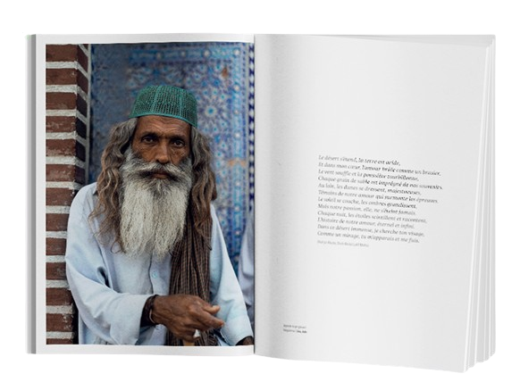 L'image représente une double page ouverte d'un livre avec une grande photographie à gauche et un texte poétique à droite.  Sur la page de gauche, une photographie en couleur montre un homme âgé avec une longue barbe blanche. Il porte une coiffe verte et une tunique claire. L'homme est appuyé contre un mur en briques, et l'arrière-plan présente une architecture ornée de carreaux bleus, typique des régions du Moyen-Orient ou d'Asie centrale. L'expression de l'homme est à la fois sage et sereine, évoquant une vie empreinte de tradition et de respect.  La page de droite est minimaliste, avec un poème ou un texte court centré. Le texte semble refléter une ambiance méditative, inspirée par la scène photographiée. Il évoque des éléments tels que le désert, la lumière, le silence et le temps, des thèmes souvent associés à la contemplation et à la sagesse des lieux anciens. Ce texte ajoute une dimension philosophique ou poétique à l'image de l'homme, renforçant l'idée d'une rencontre avec une figure symbolique de la culture ou de la spiritualité locale.  Cette mise en page crée un équilibre entre le visuel et le texte, permettant au lecteur d'apprécier à la fois l'image et la réflexion qu'elle inspire. L'ensemble invite à une immersion dans un monde à la fois visuel et intellectuel, combinant photographie et poésie.